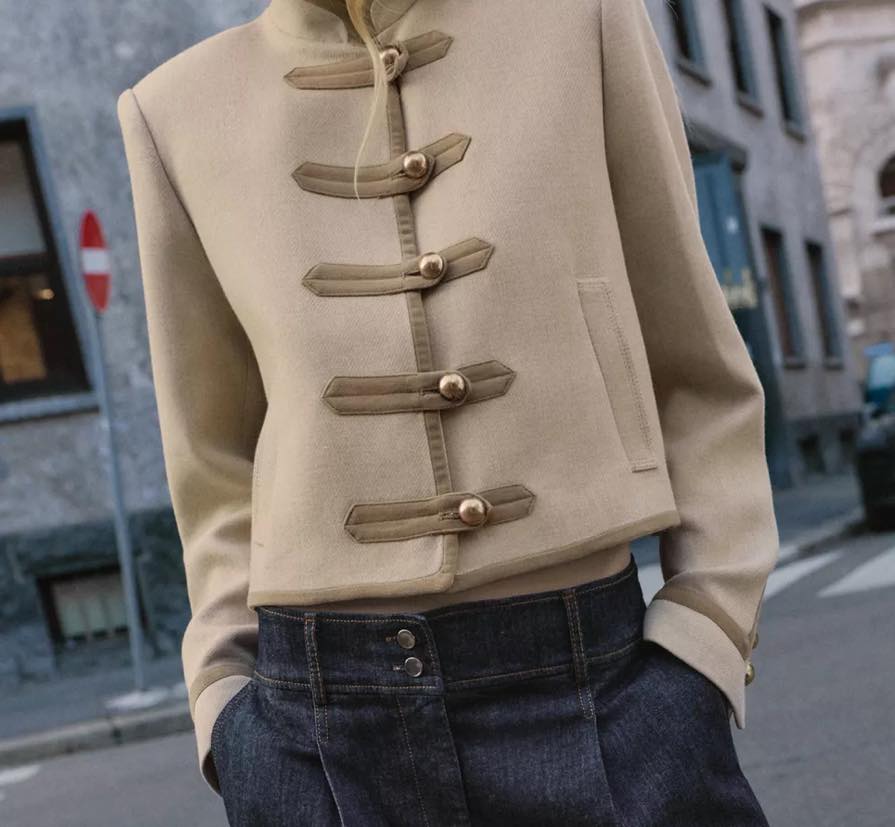Velmira Kurzjacke in Beige – Detailansicht der goldenen Knopf-Riegel mit dunkler Jeans