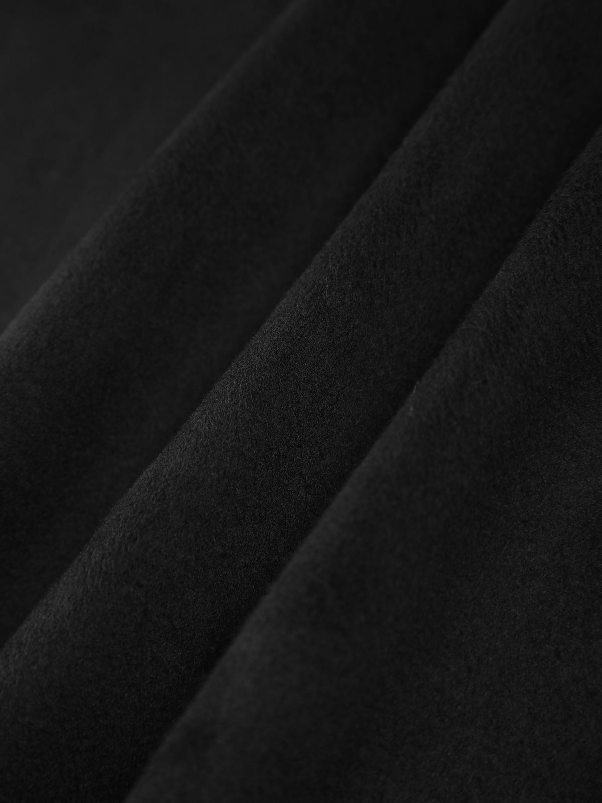 Model sitzt im schwarzen Cape-Mantel mit Schal und Taschen-Details
