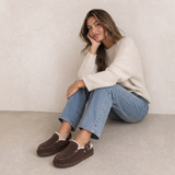 Frau in Jeans trägt dunkelbraune gefütterte Clogs im Herbst-Look