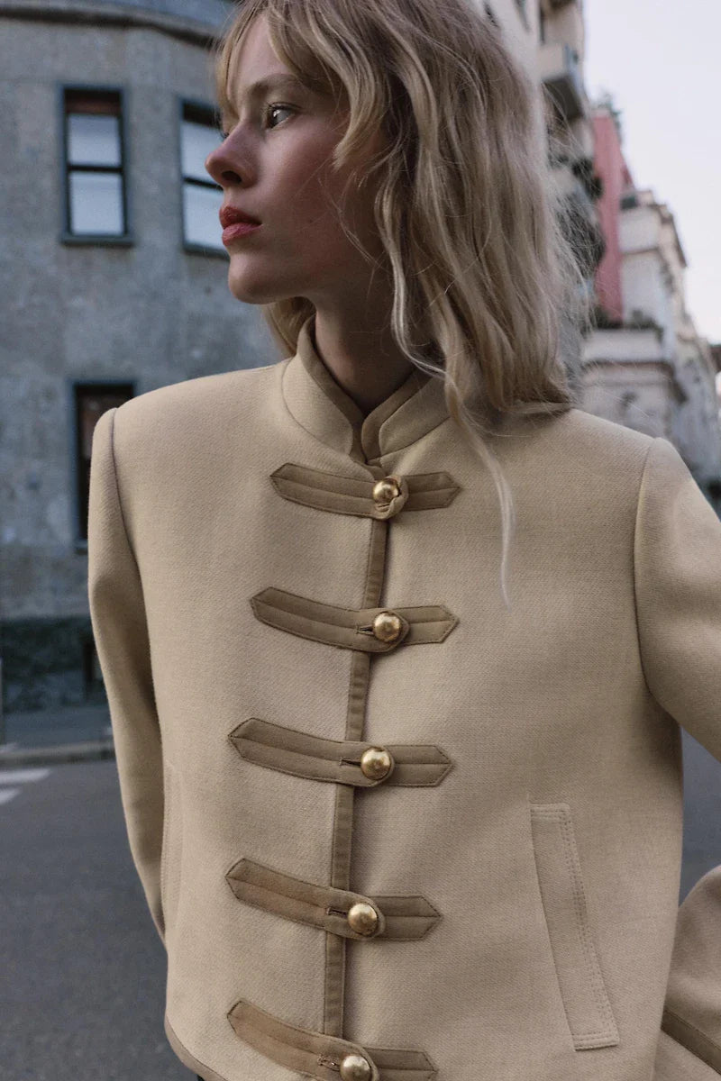 Modell trägt Velmira Taillierte Kurzjacke in Beige mit goldenen Knopf-Riegeln, Streetstyle-Aufnahme