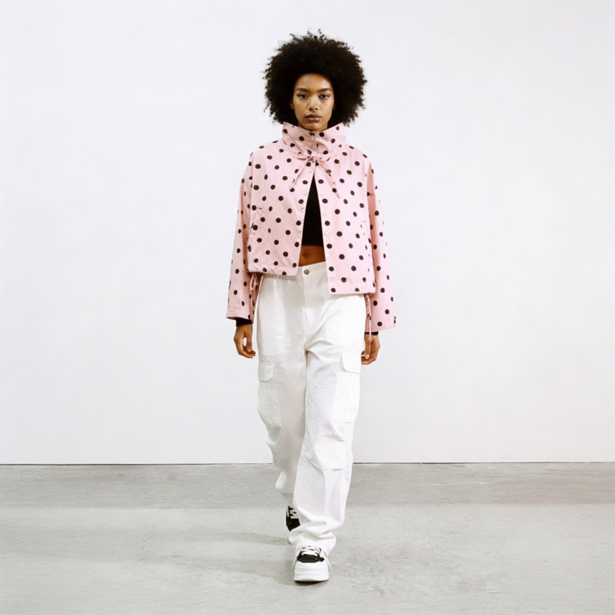 Modell trägt Rosalie Cropped Punkte-Jacke in Rosa mit schwarzen Punkten, kombiniert mit weißer Cargohose, Streetstyle-Frontansicht